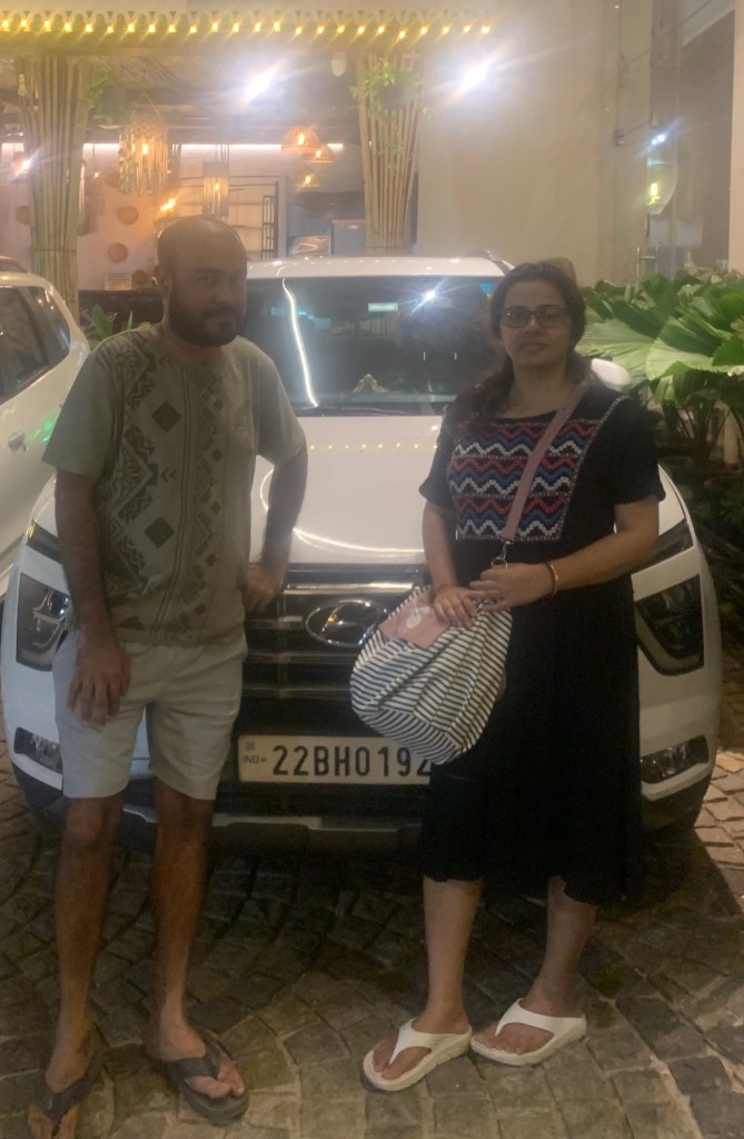 Two individuals posing in front of a white Hyundai car at night, surrounded by indoor greenery and decorative lighting.